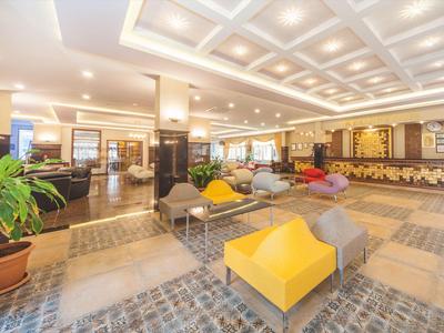 Großer, moderner Hotel-Lobbybereich mit bunten Sitzmöbeln, Pflanzen und gedämpftem Licht.