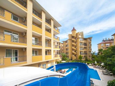 Mehrstöckige gelbe Wohngebäude mit Balkonen und blauem überdachtem Poolbereich bei sonnigem Himmel.