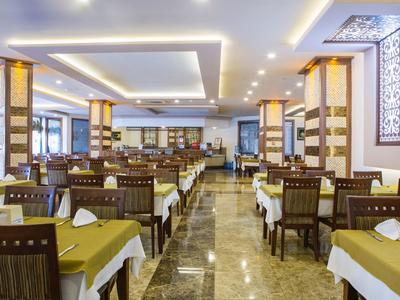 Großer, heller Speisesaal mit gedeckten Tischen, Holzstühlen und Marmorboden.