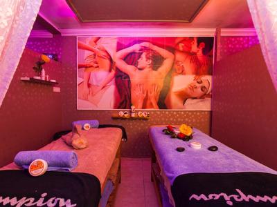 Gemütlicher Massageraum mit zwei Wellnessliegen, buntem Licht und dekorativem Wandbild.