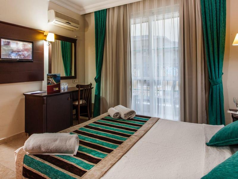 Gemütliches Schlafzimmer mit Doppelbett, grün-weißer Bettwäsche, Schreibtisch und Balkon mit Vorhängen.