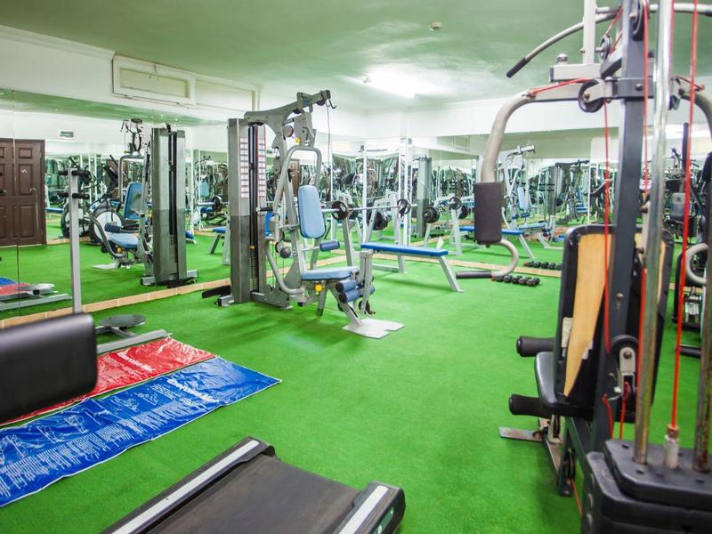 Fitnessstudio mit grünen Boden, Trainingsgeräten, Spiegeln an den Wänden und Trainingsmatten.