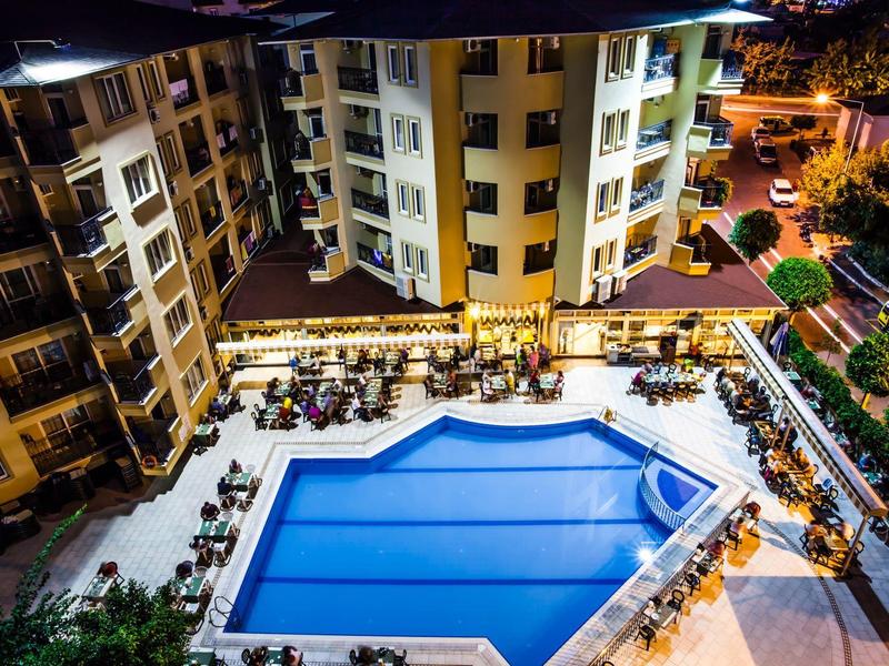 Beleuchteter Swimmingpool inmitten eines Hotels bei Nacht mit umliegenden Sitzbereichen und Pflanzen.