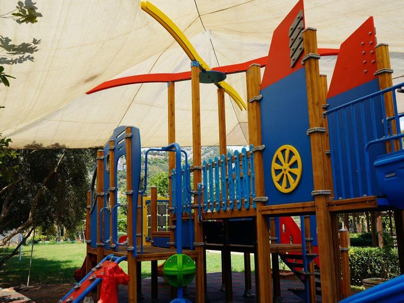 Bunter Spielplatz mit Rutsche, Klettergerüst und Sonnensegel im Freien bei Tageslicht.