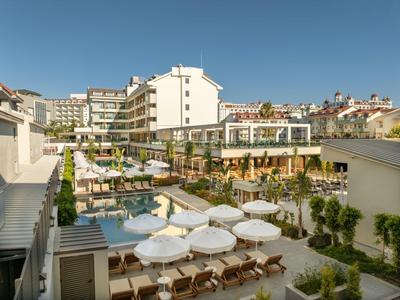 Nowoczesny hotel z basenem, parasolami i leżakami pod czystym niebieskim niebem.