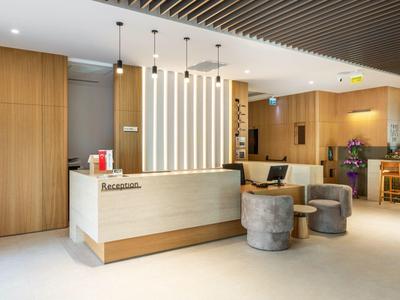 Nowoczesna recepcja hotelowa z jasnym biurkiem, drewnianymi ścianami i przytulnym miejscem do siedzenia.