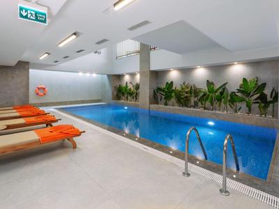 Piscine intérieure moderne avec transats et plantes le long du mur dans un hôtel.