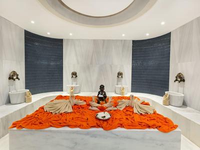 Luksusowy pokój spa z białym marmurem, przytłumionym oświetleniem i pomarańczowym ręcznikiem na stole