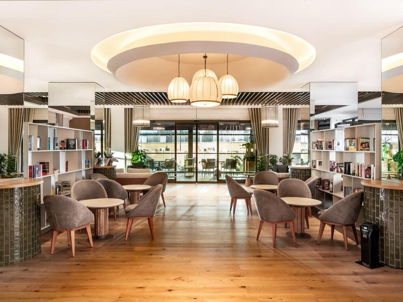 Jasno urządzona poczekalnia hotelowa z fotelami, okrągłymi lampami i drewnianą podłogą.