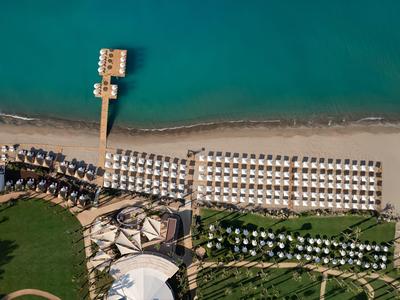 Luftaufnahme eines Strandes mit Sonnenschirmen, Liegen, Steg und angrenzendem Hotelgarten.