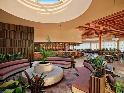 Großzügige Hotellobby mit runden Sitzbereichen, Pflanzen und natürlichem Licht durch Kuppel.
