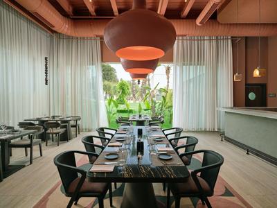 Modernes Hotelrestaurant mit großem Holztisch, Stühlen und großen Hängeleuchten.