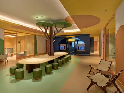 Moderner Hotel-Loungebereich mit langem Holztisch, Baumdeko und gemütlichen Sitzgelegenheiten.