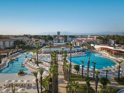 Großer Hotelpoolbereich mit Sonnenliegen, Palmen und moderner Hotelanlage im Hintergrund.