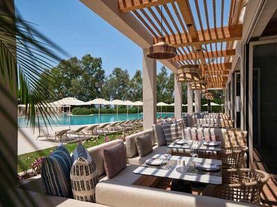 Moderne Hotelterrasse mit Sitzgelegenheiten, Sonnenschirmen und Blick auf den Pool und Garten.