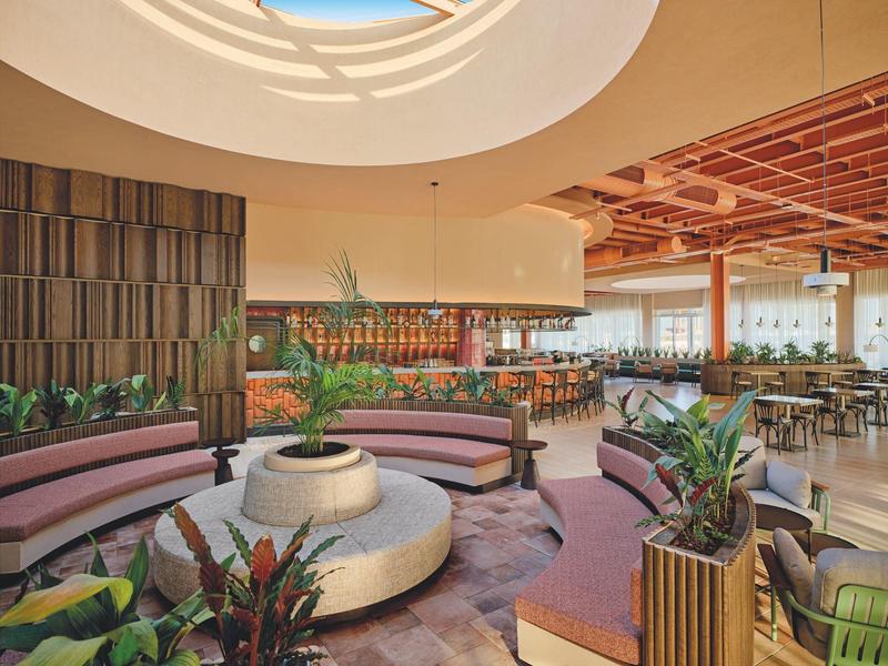 Modernes Hotel-Lounge mit runder Sitzecke, Pflanzen und natürlichem Licht von einem Oberlicht