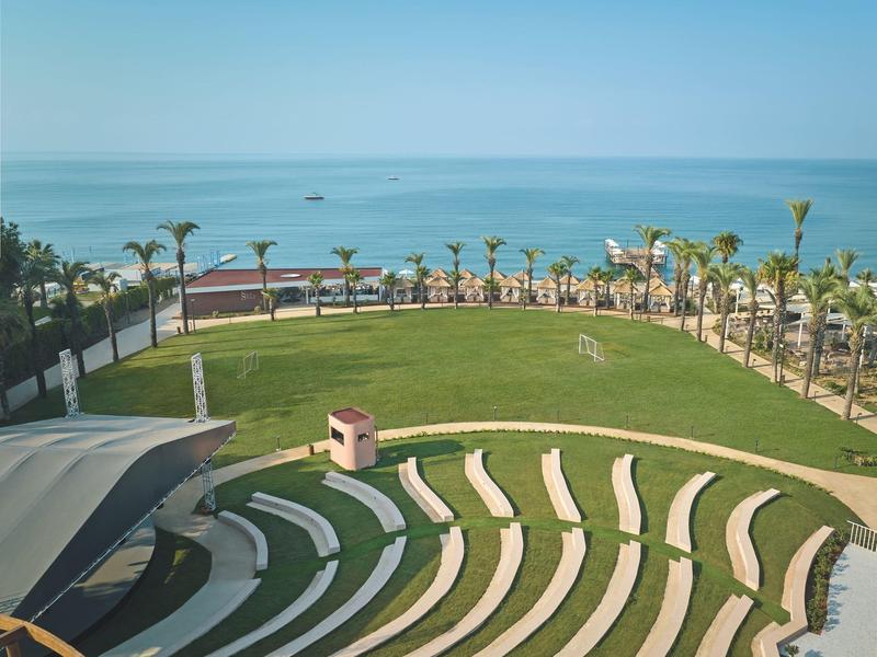 Grüne Rasenfläche mit geschwungenen weißen Sitzreihen und Blick auf das Meer.
