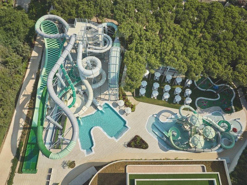 Luftaufnahme eines Wasserparks mit mehreren Wasserrutschen und Pools, umgeben von Bäumen.