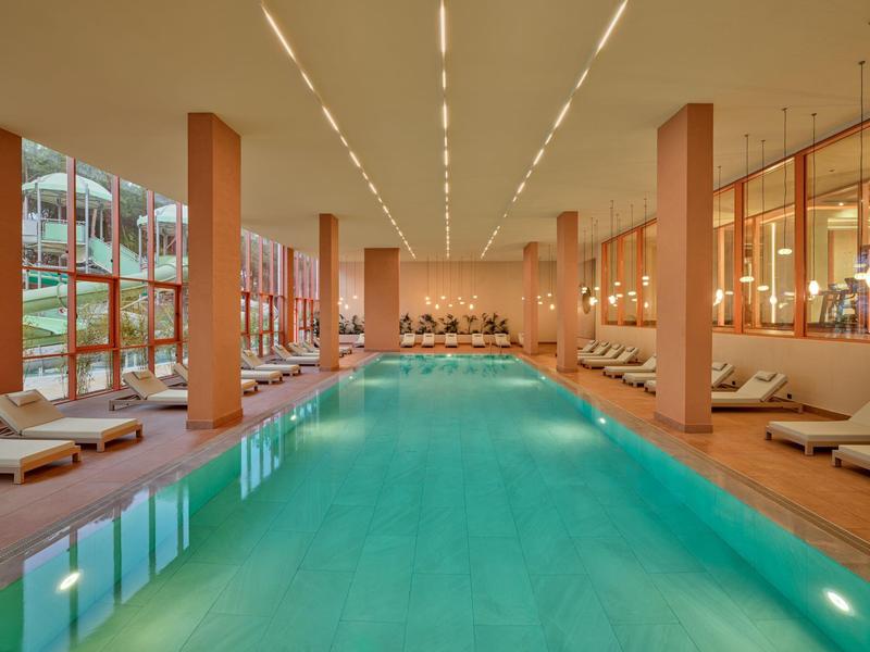 Großes, modernes Hallenbad mit Liegestühlen und warmem Licht in einem Hotel.