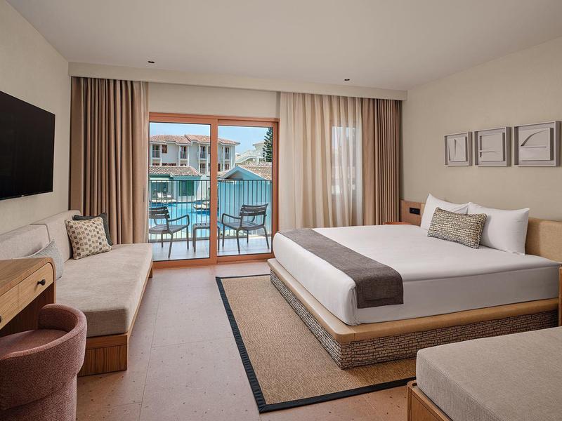 Modernes Hotelzimmer mit zwei Betten, Balkon und Blick auf den Pool.