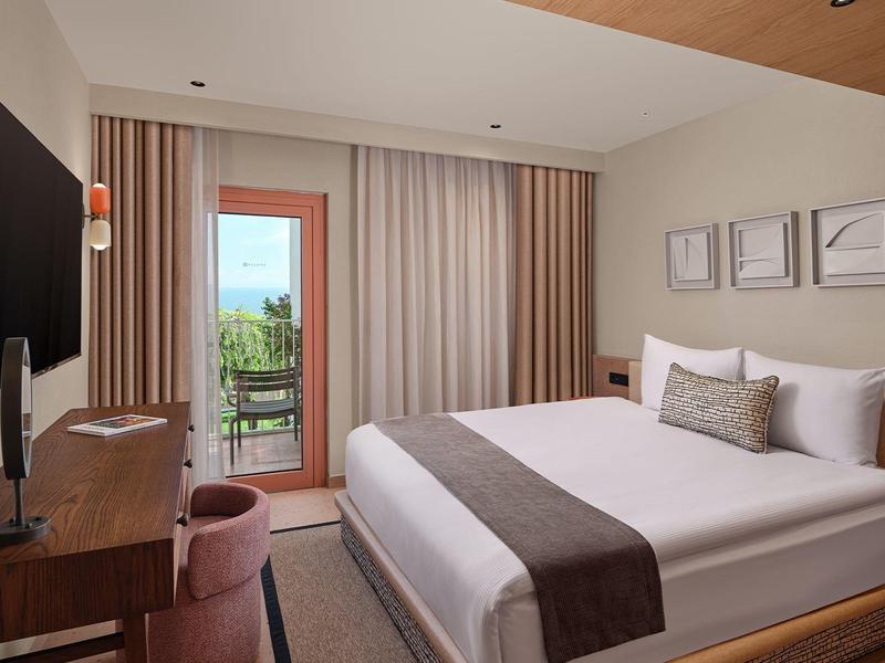 Modernes Hotelzimmer mit großem Bett, TV, Balkon und neutraler Dekoration.