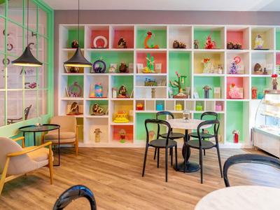 Buntes Café mit Holzboden, Regalen voller Dekoration und verschiedenen Sitzgelegenheiten.