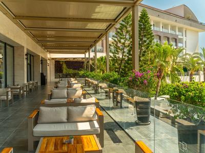 Terrassenbereich mit Sofas, Tischen, Sonnendach und grünem Garten vor einem modernen Gebäude.