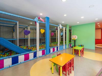 Innenraum eines bunten Kinderspielbereichs mit Bällebad, Rutsche, kleinen Tischen und Stühlen.