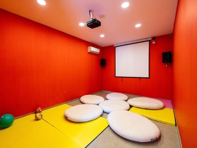 Ein Raum mit roten Wänden, gelbem Boden, weißen Polstern und einer Projektionsleinwand.