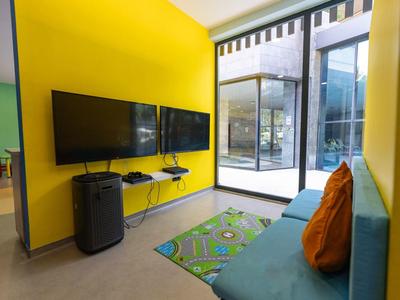 Modernes Wartezimmer mit gelben Wänden, blauer Couch, orangen Kissen und zwei Fernsehern an der Wand.