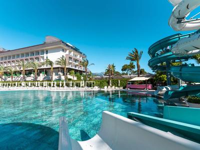 Moderní hotelový komplex s bazénem, tobogány a palmami pod modrou oblohou.