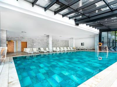 Ein großer, rechteckiger Hallenbad mit glasklarem Wasser, Liegestühlen und Glasdach.