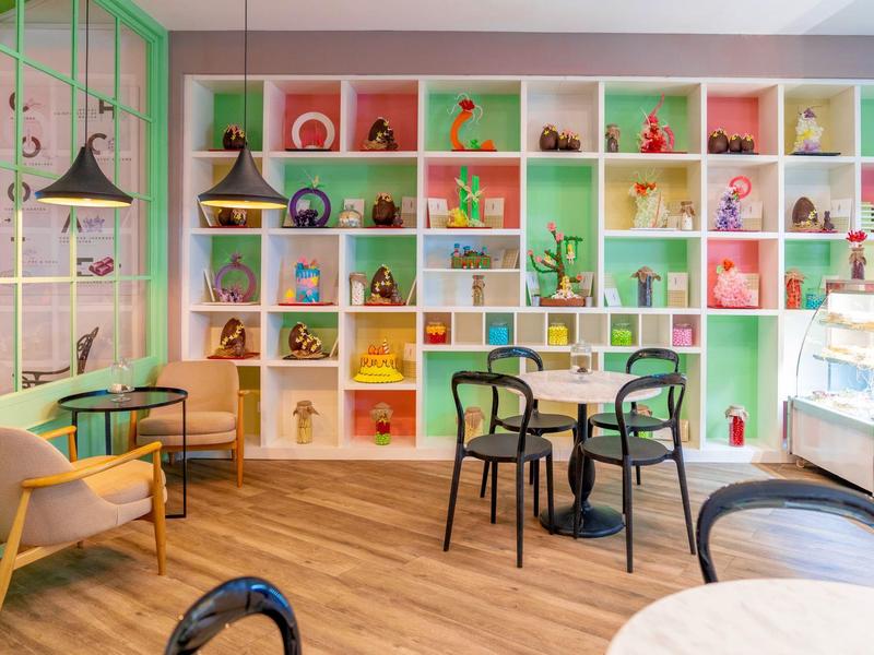 Buntes Café mit Holzboden, Regalen voller Dekoration und verschiedenen Sitzgelegenheiten.