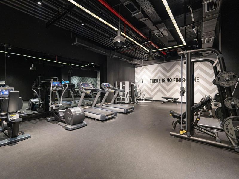 Moderner Fitnessraum mit Laufbändern, Fahrrädern, Gewichten und schwarzer Decke mit roter Beleuchtung.