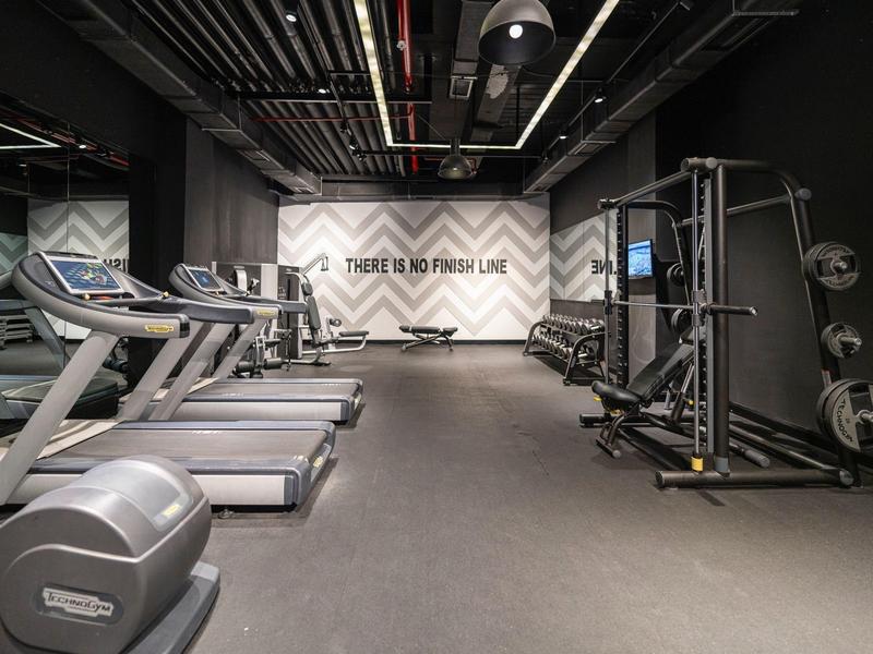 Moderner Fitnessraum mit Laufbändern, Kraftmaschinen und einem Spruch an der Wand.