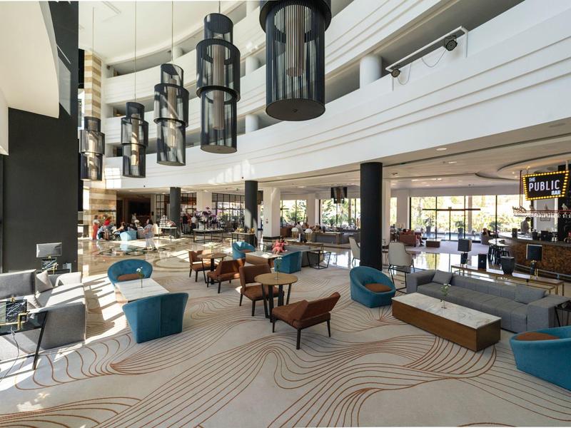 Großer moderner Lobbybereich mit Sitzgruppen, Holztischen, blauen Sitzhockern und Hängelampen.