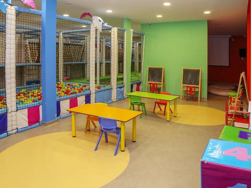 Bunter Indoor-Spielbereich mit Tischtennis, Ballbad und kleinen Tischen mit Stühlen.