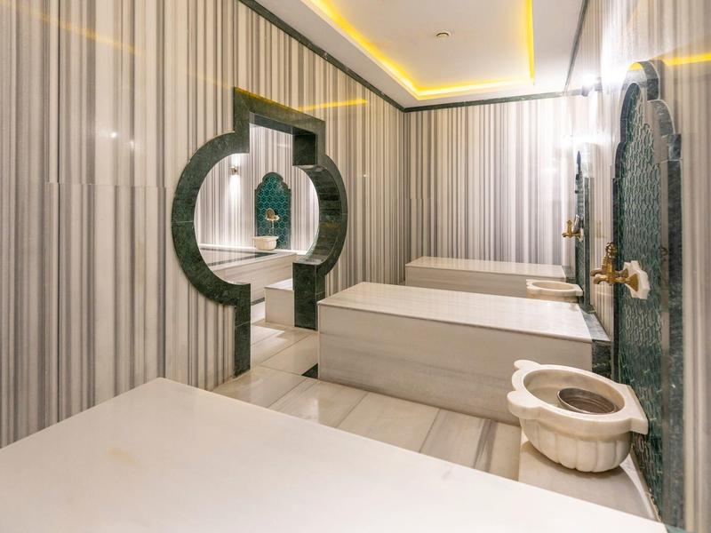 Moderner Hamam mit Marmorliegen, großem Spiegel und schlanken Kerzenständern an der Wand.