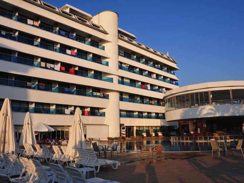 Modernes Hotelgebäude mit mehreren Balkonen und Sonnenschirmen am Poolbereich bei Sonnenuntergang.