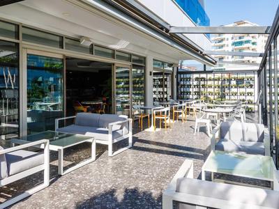 Moderne Terrasse mit weißen Sitzmöbeln, Glaswänden und Blick auf umliegende Gebäude.