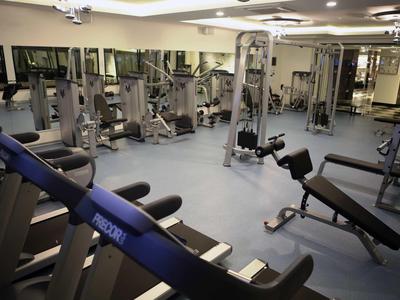 Fitnessraum mit Trainingsgeräten wie Laufbändern, Gewichten und Kabelzügen in hellem Raum.