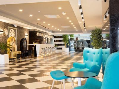 Moderner Hotel-Lobby mit schwarz-weißem Boden, blauen Sesseln, Bar und grünen Pflanzen.