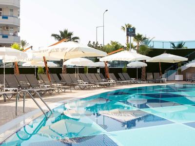 Großer Schwimmbad mit klarem blauem Wasser, weißen Sonnenschirmen und Reihen von Liegestühlen.