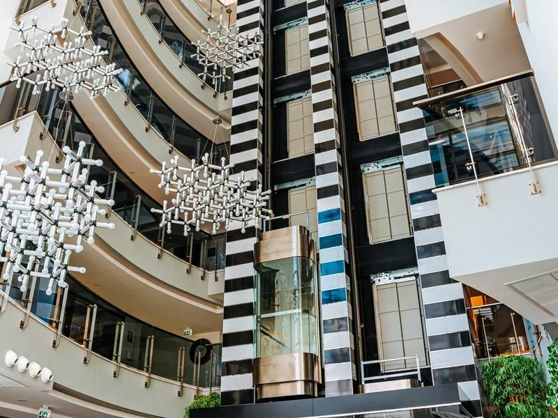 Ascensor moderno en un atrio de hotel de varios pisos con diseño en vidrio y blanco y negro.