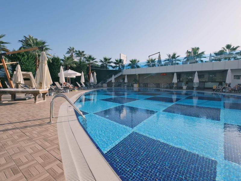 Gran piscina de hotel con azulejos azules, rodeada de tumbonas y palmeras.