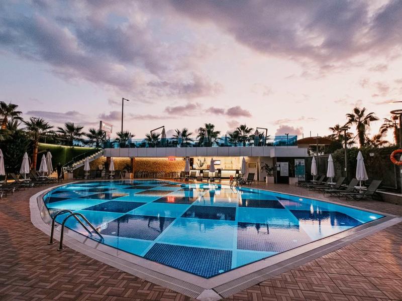 Piscina redonda al aire libre al atardecer con tumbonas y palmeras al fondo.