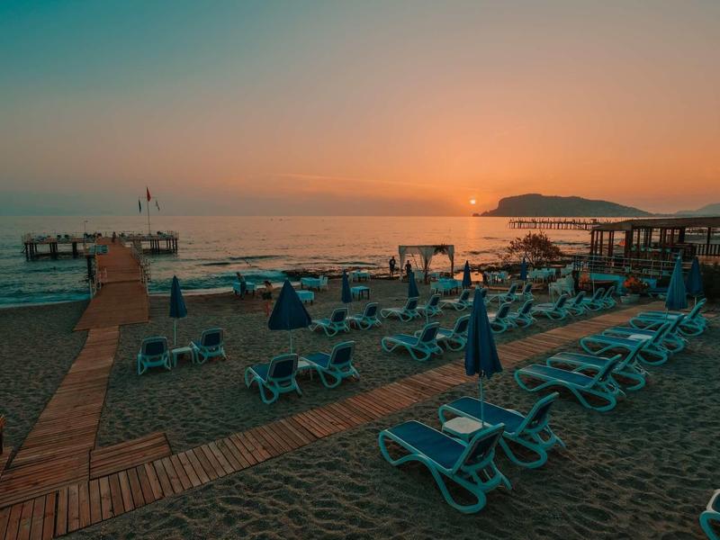 Puesta de sol en la playa con hamacas vacías y pasarelas de madera hacia el agua.