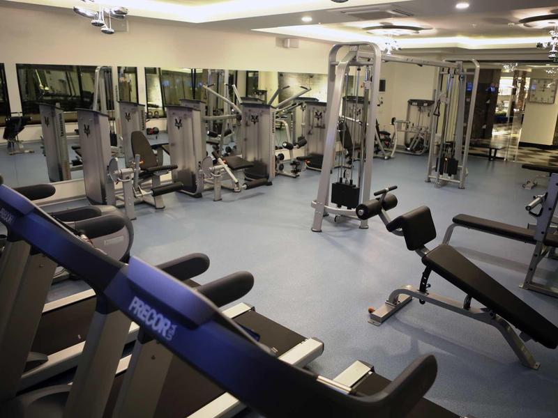 Sala de gimnasio con varias máquinas de ejercicio y pesas en suelo limpio y luces brillantes.