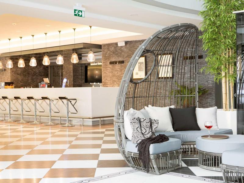 Interior de hotel con barra de bar moderna y sillón de mimbre grande junto a mesa baja redonda.