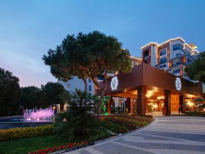 Hotel moderno con entrada iluminada y fuente al atardecer.